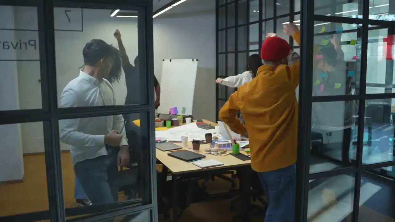 Team brainstorming in a glass-walled meeting room with sticky notes and design materials on the table