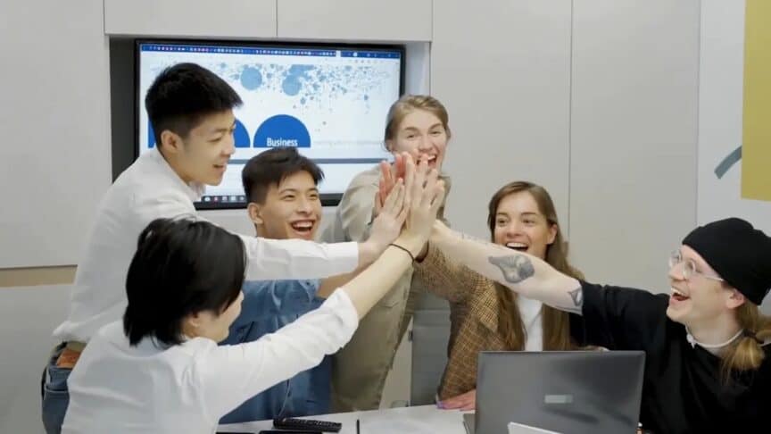 A small team giving a group high-five around a laptop in a meeting room