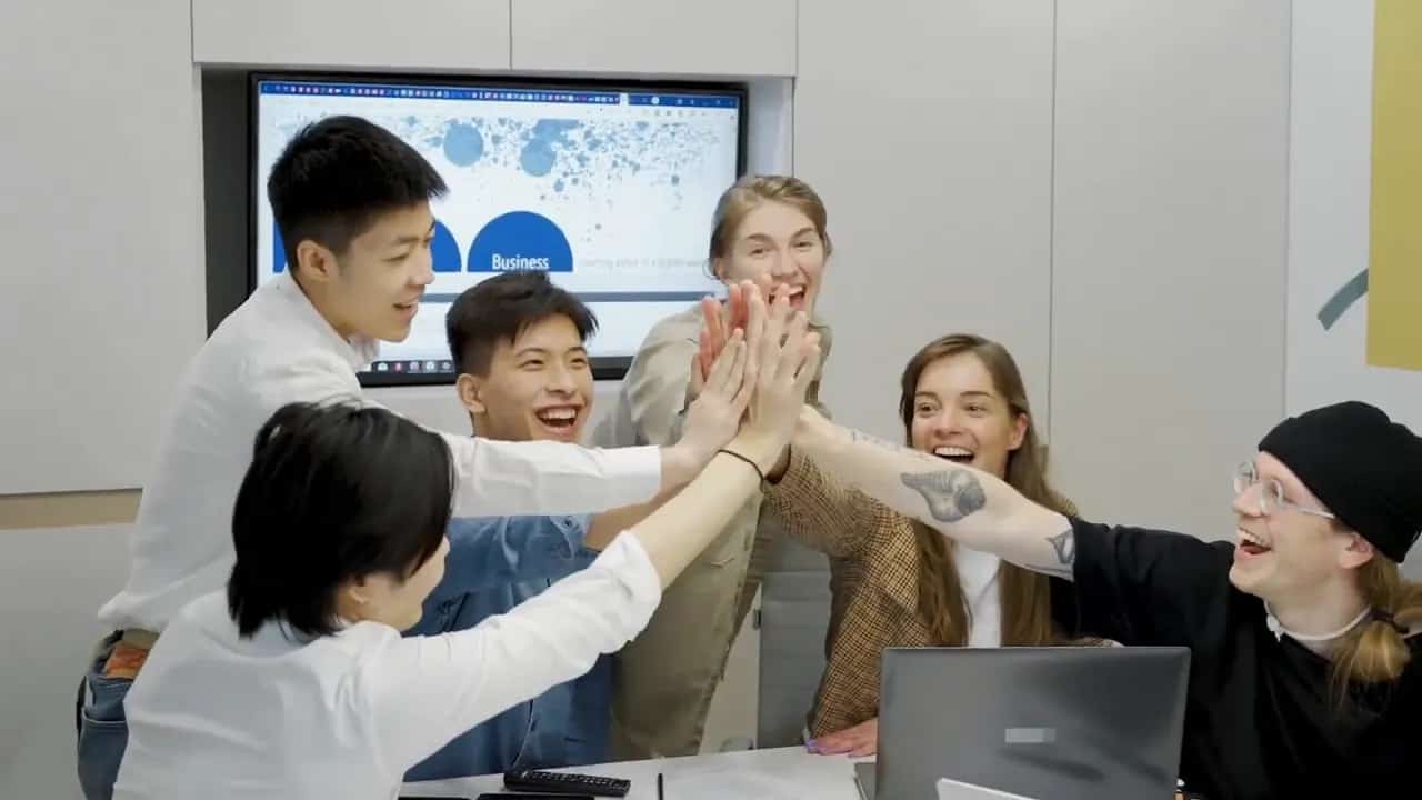 A small team giving a group high-five around a laptop in a meeting room